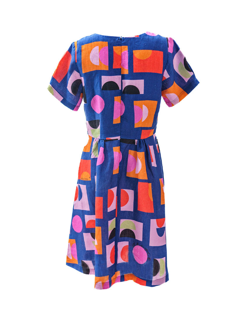 DEVOI Audrina Dress in Just Pretend Blue printed linen. A new version of best selling Dorothy dress. With a blue background and red, orange and pink accents. Back view.