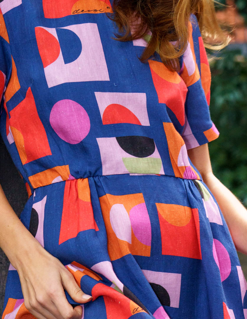 DEVOI Audrina Dress in Just Pretend Blue printed linen. A new version of best selling Dorothy dress. With a blue background and red, orange and pink accents. Close-up fabric view