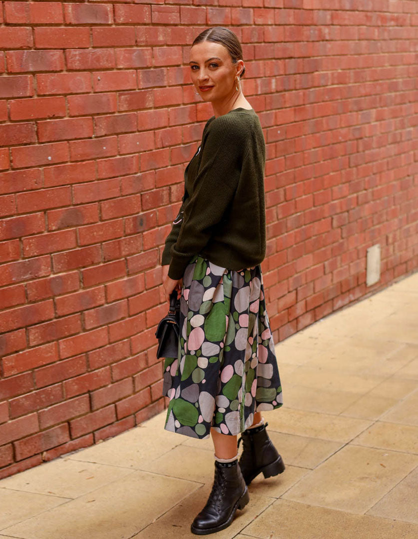 DEVOI Printed Kathleen linen skirt in a green pebbles print. Midi length with pocket and an elasticated waistband. Side view on model