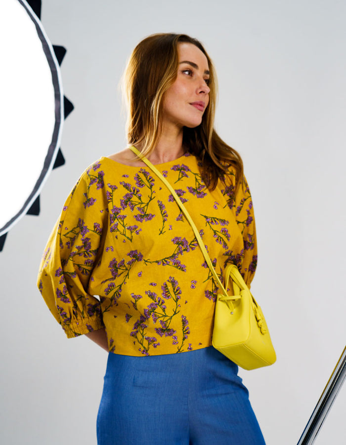 DEVOI Scalavender printed linen top with batwing sleeves. Boat neckline. Mustard and purple print. Side Front view on model.